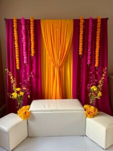 Mehndi ceremony setup with vibrant drapes, floral arrangements, and a cozy seating area on the stage.